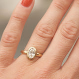 chunky gold engagement ring with stepped double bezel holding an oval diamond on a hand with red nail polish.