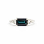 white gold engagement ring with east-to-west dark blue sapphire and diamonds on a white background