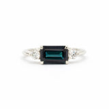 white gold engagement ring with east-to-west dark blue sapphire and diamonds on a white background