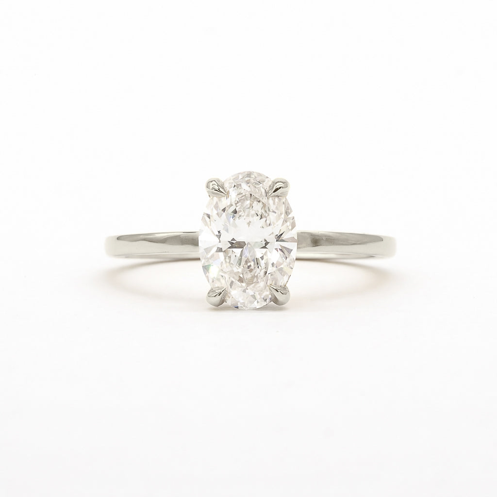An oval-cut diamond solitaire ring in a four-prong setting on a polished silver-colored band, centered against a plain white background.