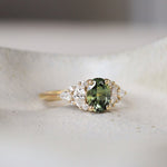 Ring with a green gemstone and 12-stone diamond cluster on a white surface
