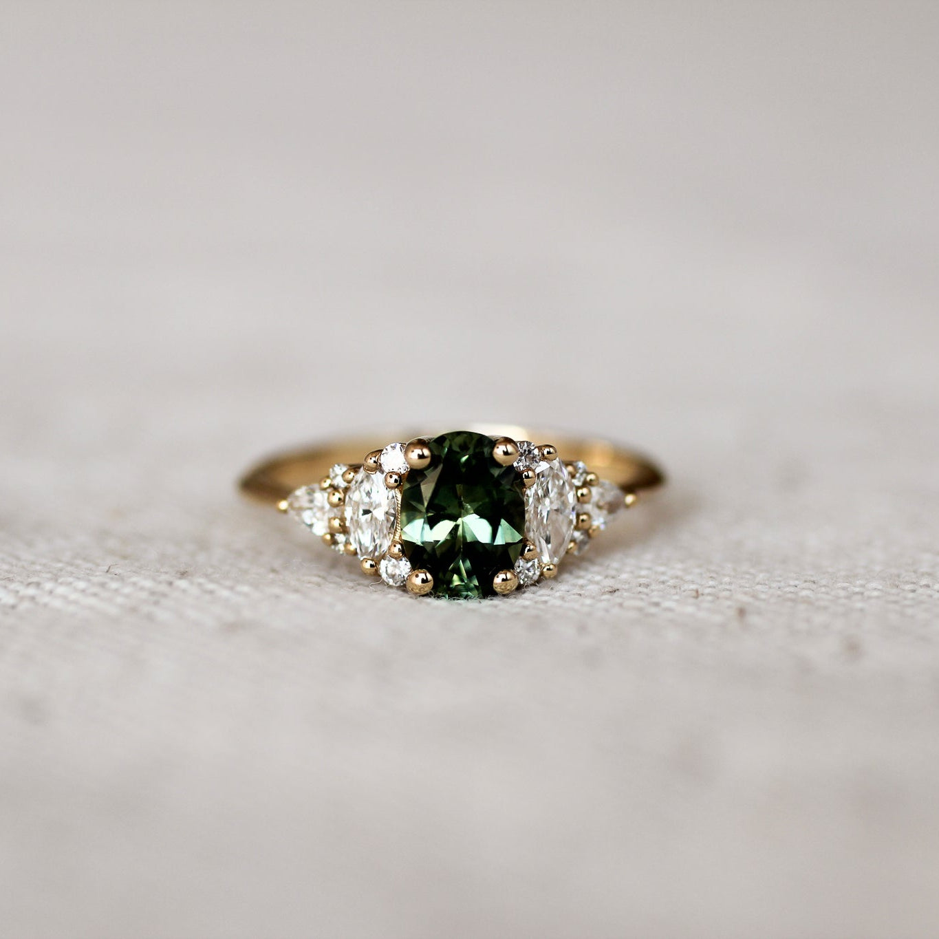 Gold ring with a green gemstone and 12 marquise, round and pear diamonds on a textured surface