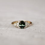 Gold ring with a green gemstone and 12 marquise, round and pear diamonds on a textured surface