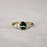 Gold ring with a green gemstone and 12 marquise, round and pear diamonds on a textured surface
