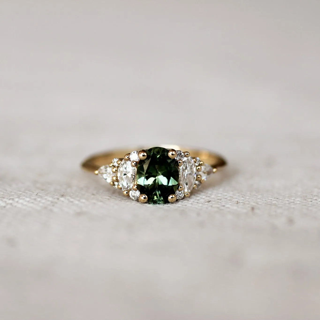 Gold ring with a green gemstone and 12 marquise, round and pear diamonds on a textured surface