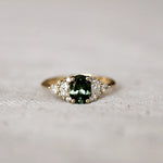 Gold ring with a green gemstone and 12 marquise, round and pear diamonds on a textured surface