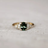 Gold ring with a green gemstone and 12 marquise, round and pear diamonds on a textured surface