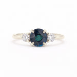 A silver-tone ring featuring a round-cut dark blue sapphire center stone flanked by two small round-cut clear diamonds on a white background.