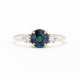 A silver-tone ring featuring a round-cut dark blue sapphire center stone flanked by two small round-cut clear diamonds on a white background.