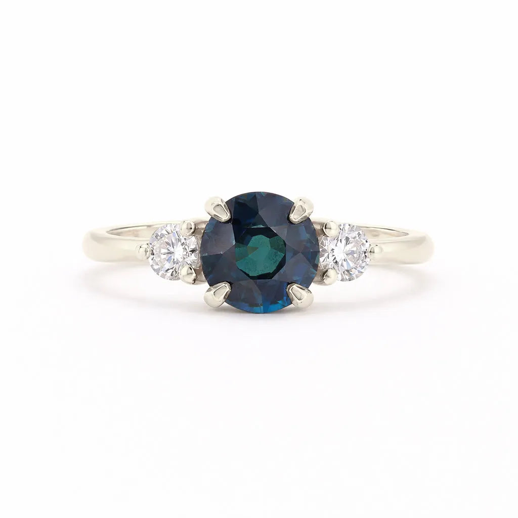 A silver-tone ring featuring a round-cut dark blue sapphire center stone flanked by two small round-cut clear diamonds on a white background.