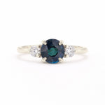 A silver-tone ring featuring a round-cut dark blue sapphire center stone flanked by two small round-cut clear diamonds on a white background.