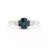 A silver-tone ring featuring a round-cut dark blue sapphire center stone flanked by two small round-cut clear diamonds on a white background.