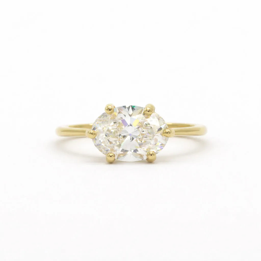 east-west set diamond engagement ring with oval diamond in gold on a white background