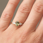 Close-up of a hand wearing a ring with a green gemstone on a neutral background