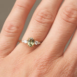 Close-up of a hand wearing a ring with a green gemstone on a neutral background