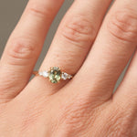 Close-up of a hand wearing a ring with a green gemstone on a neutral background