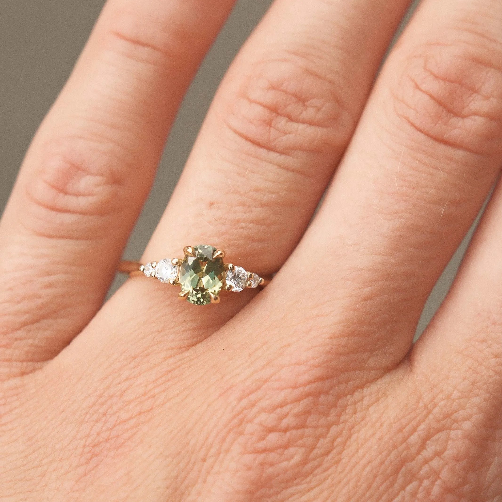 Close-up of a hand wearing a ring with a green gemstone on a neutral background