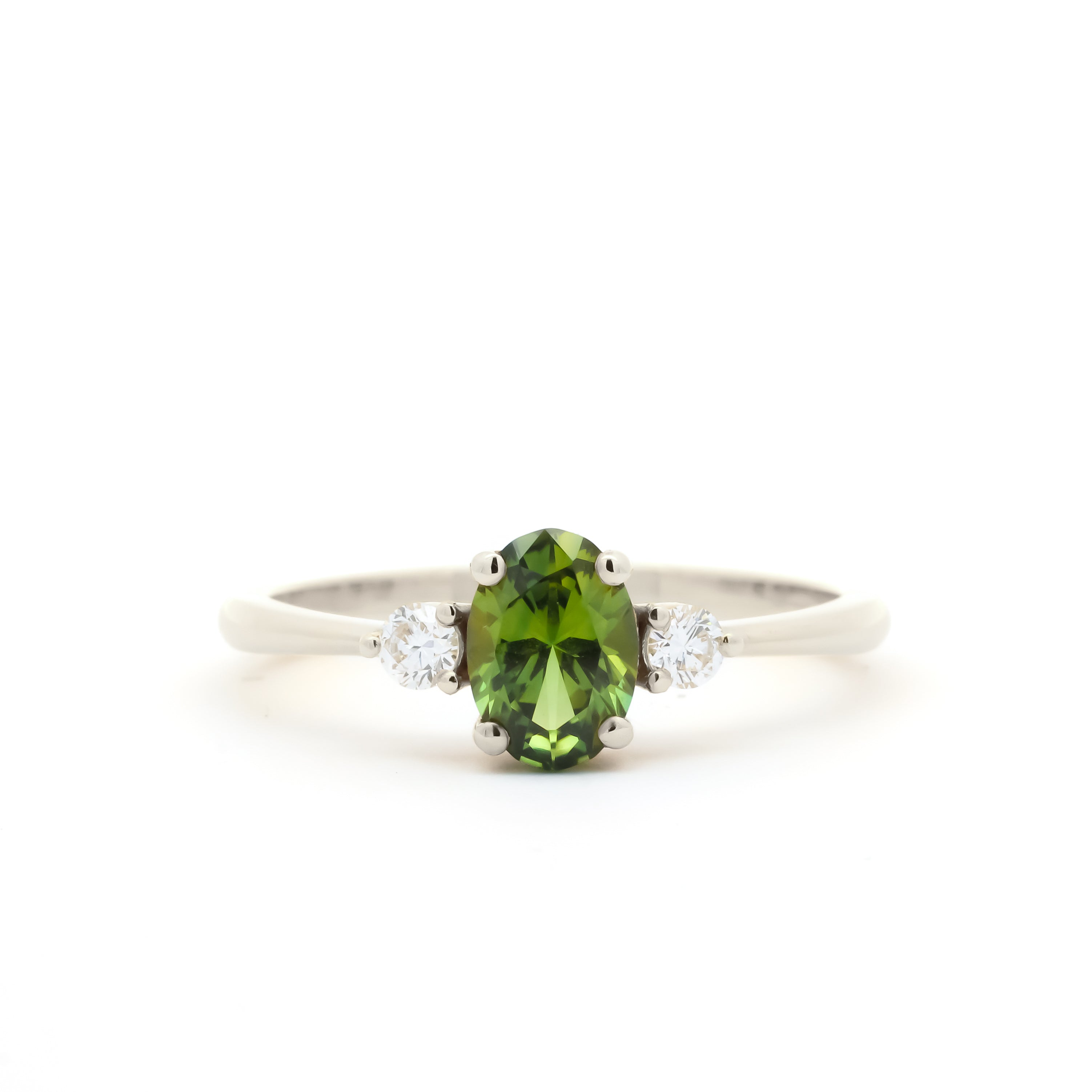 A white-gold three-stone ring featuring a central oval-cut green peridot gemstone flanked by two small round-cut clear diamonds, set against a plain white background.