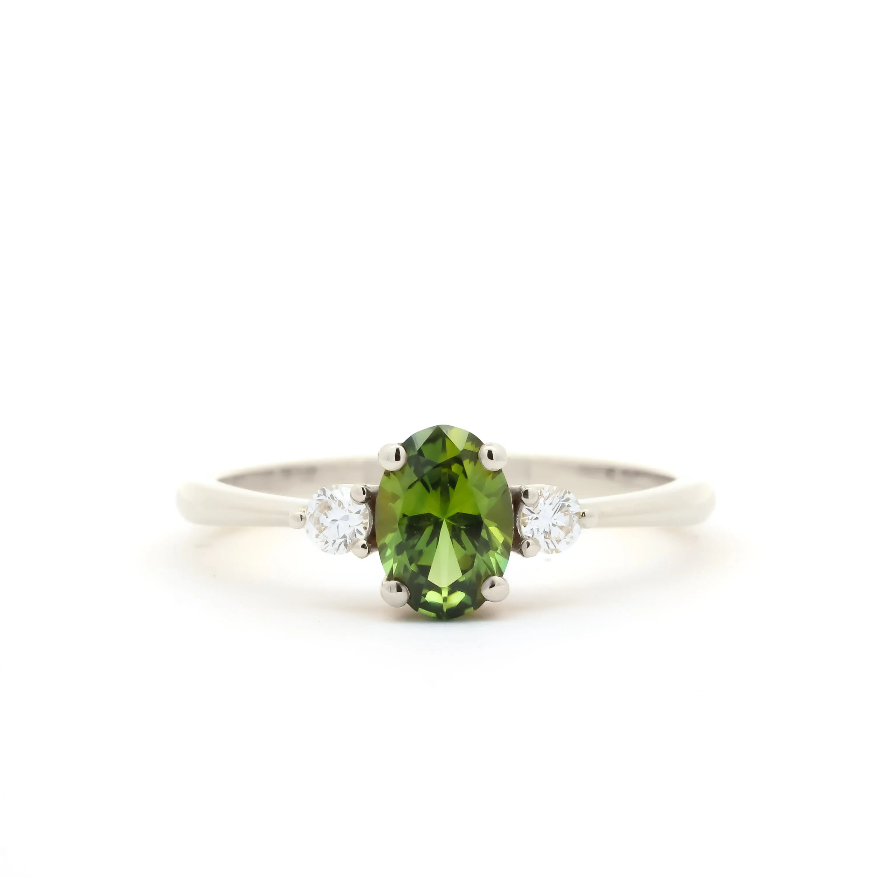 A white-gold three-stone ring featuring a central oval-cut green peridot gemstone flanked by two small round-cut clear diamonds, set against a plain white background.