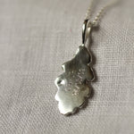 Silver leaf-shaped pendant with 'CH + JH 24/03/09' engraved on a chain against a neutral background