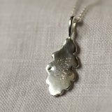 Silver leaf-shaped pendant with 'CH + JH 24/03/09' engraved on a chain against a neutral background