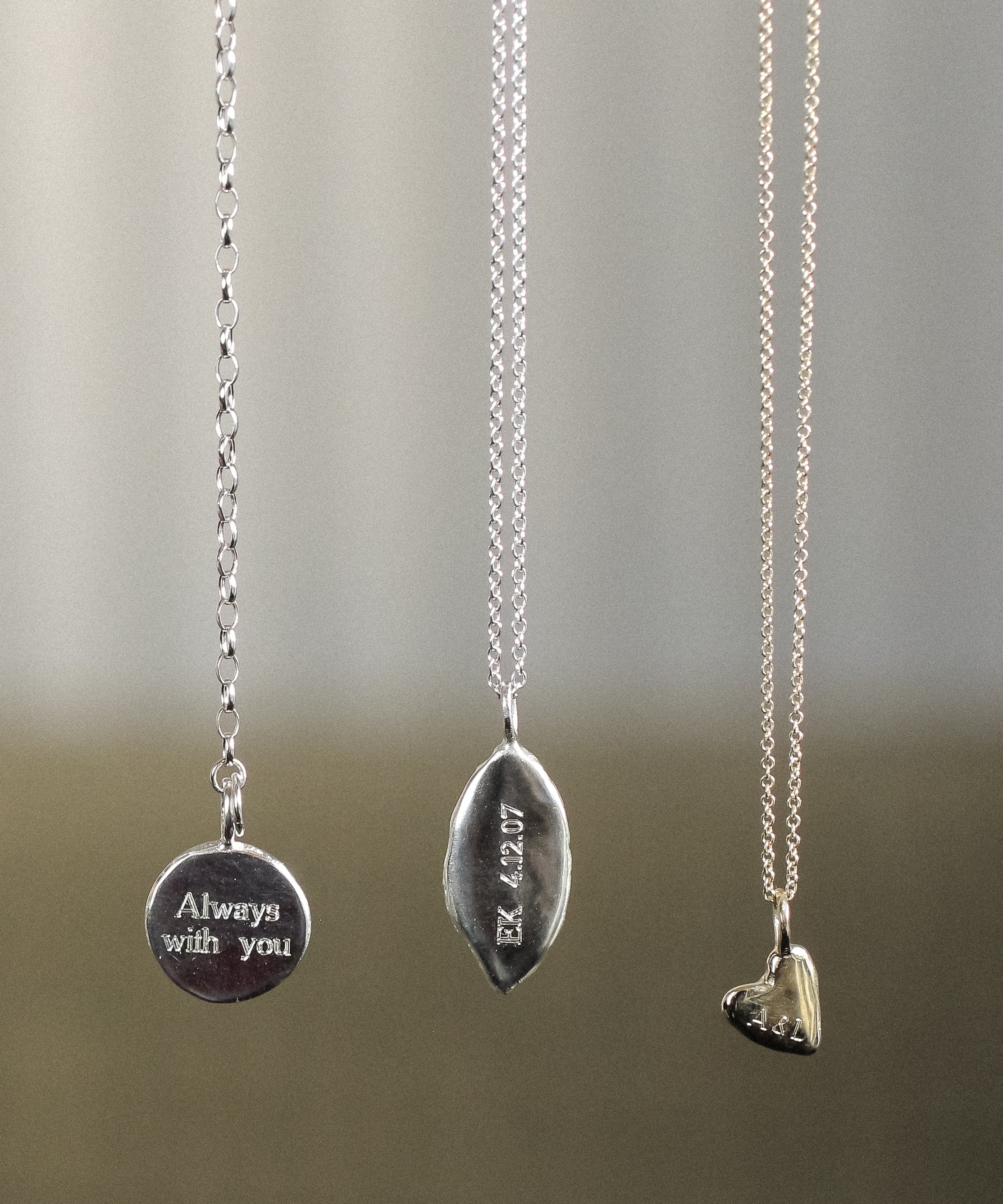 Three silver necklaces with engraved pendants on a neutral background