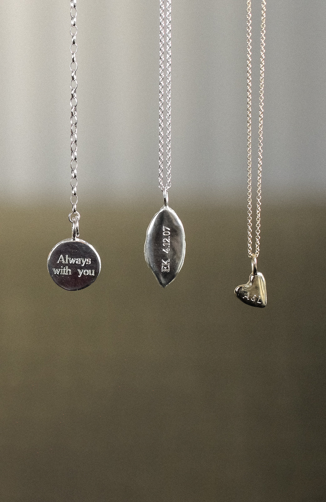 Three silver necklaces with engraved pendants on a neutral background