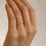 Hand wearing a thin 1mm yellow gold 3/4 eternity wedding ring on a plain background