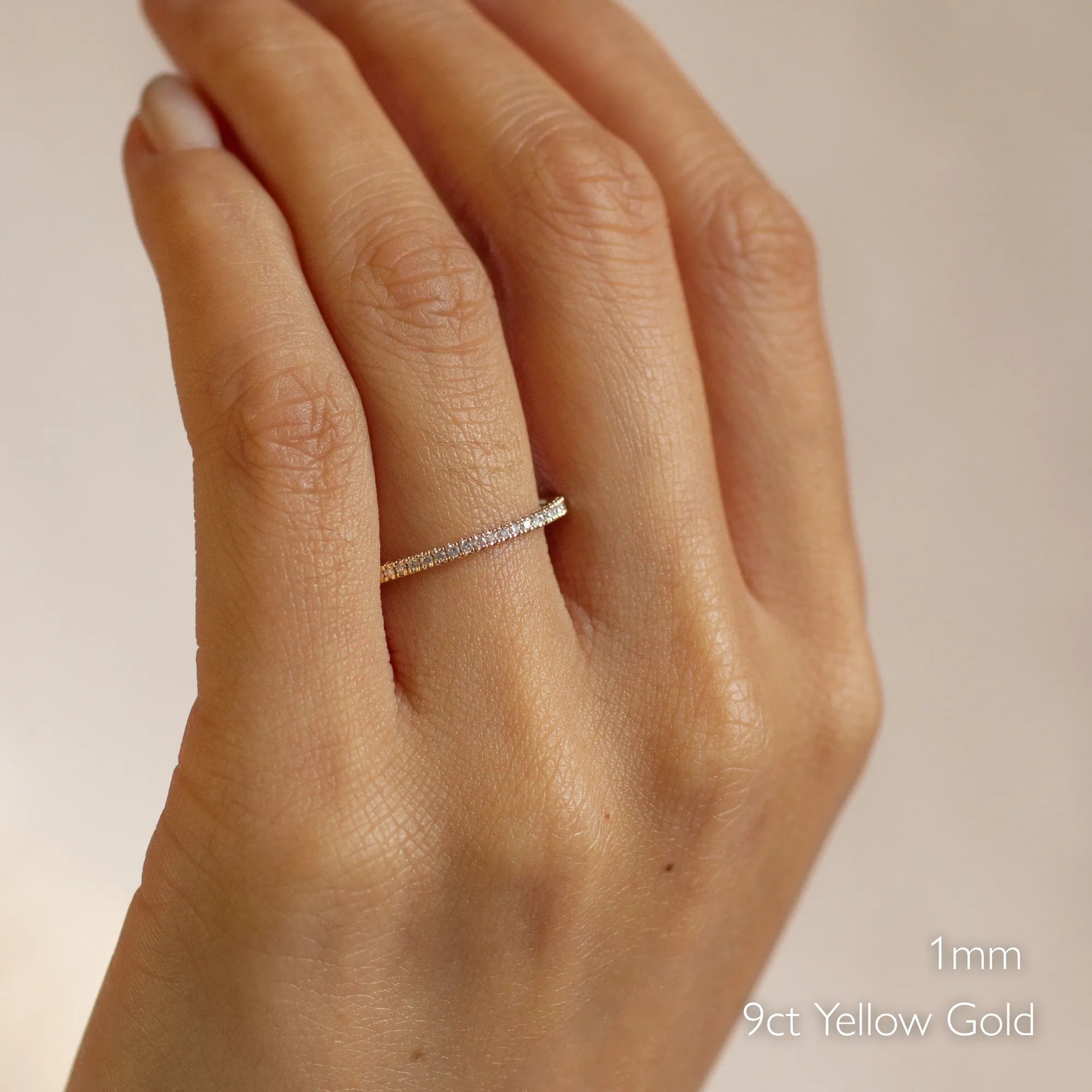 Hand wearing a thin 1mm yellow gold 3/4 eternity wedding ring on a plain background