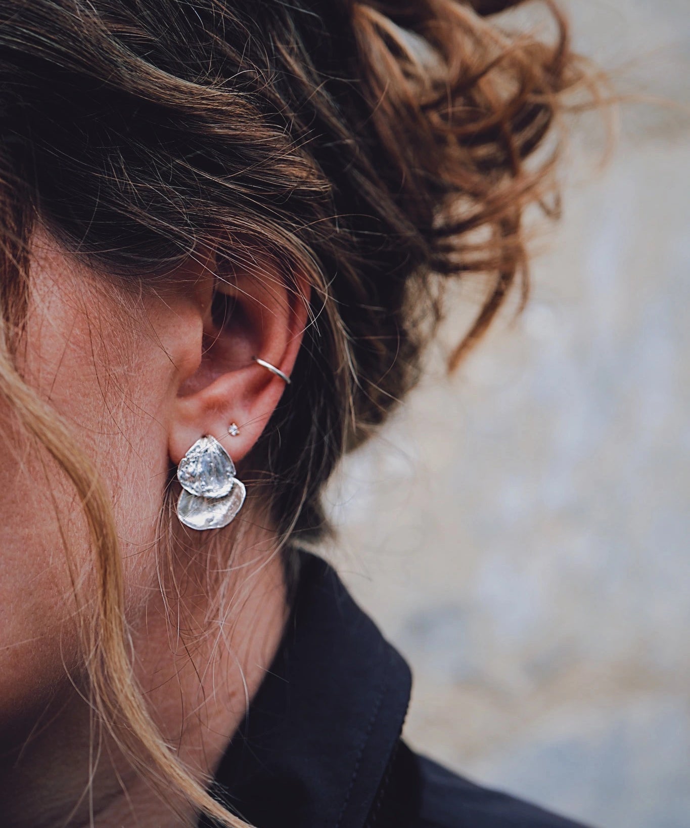 close up of brunette girl wearing silver petal drop earrings, diamond stud and ear cuff