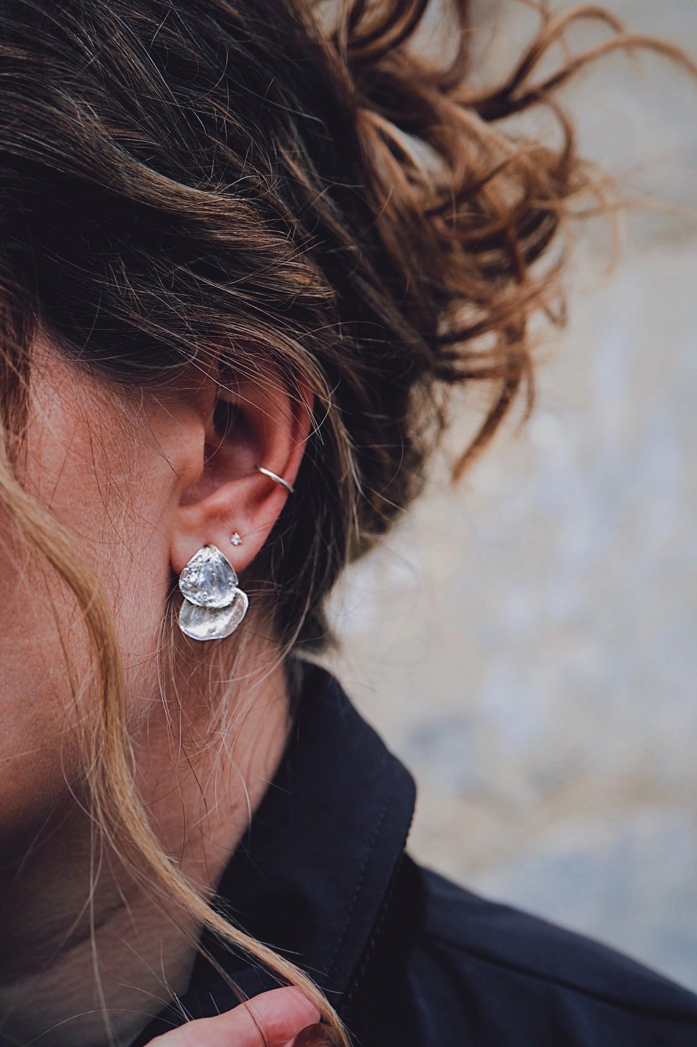 close up of brunette girl wearing silver petal drop earrings, diamond stud and ear cuff