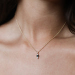 A close-up of a delicate gold chain necklace with a small teardrop-shaped pendant featuring a dark green stone, worn on a model's neck.