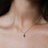 A close-up of a delicate gold chain necklace with a small teardrop-shaped pendant featuring a dark green stone, worn on a model's neck.