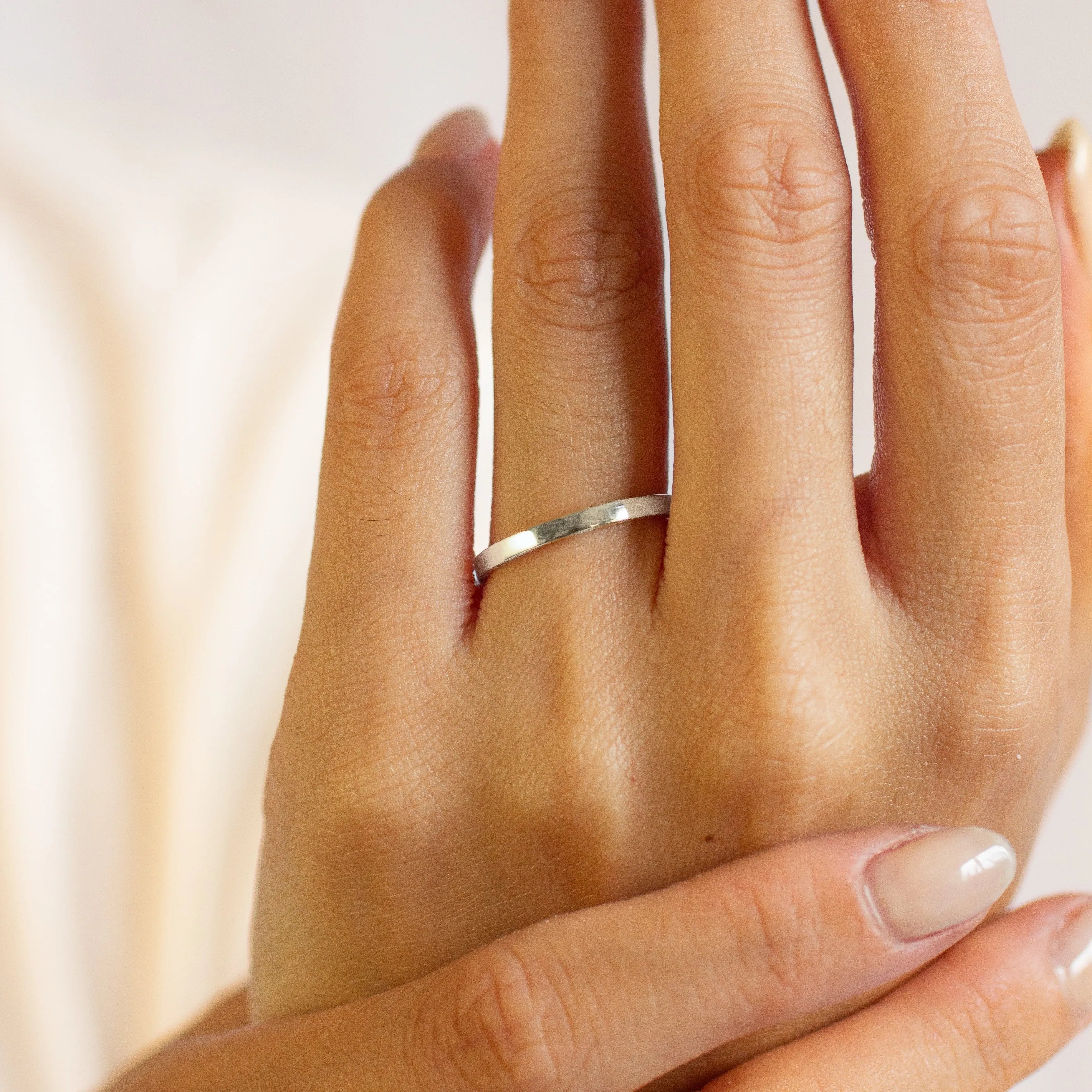 Close-up of a hand wearing a flat 2mm white gold wedding ring with a blurred background