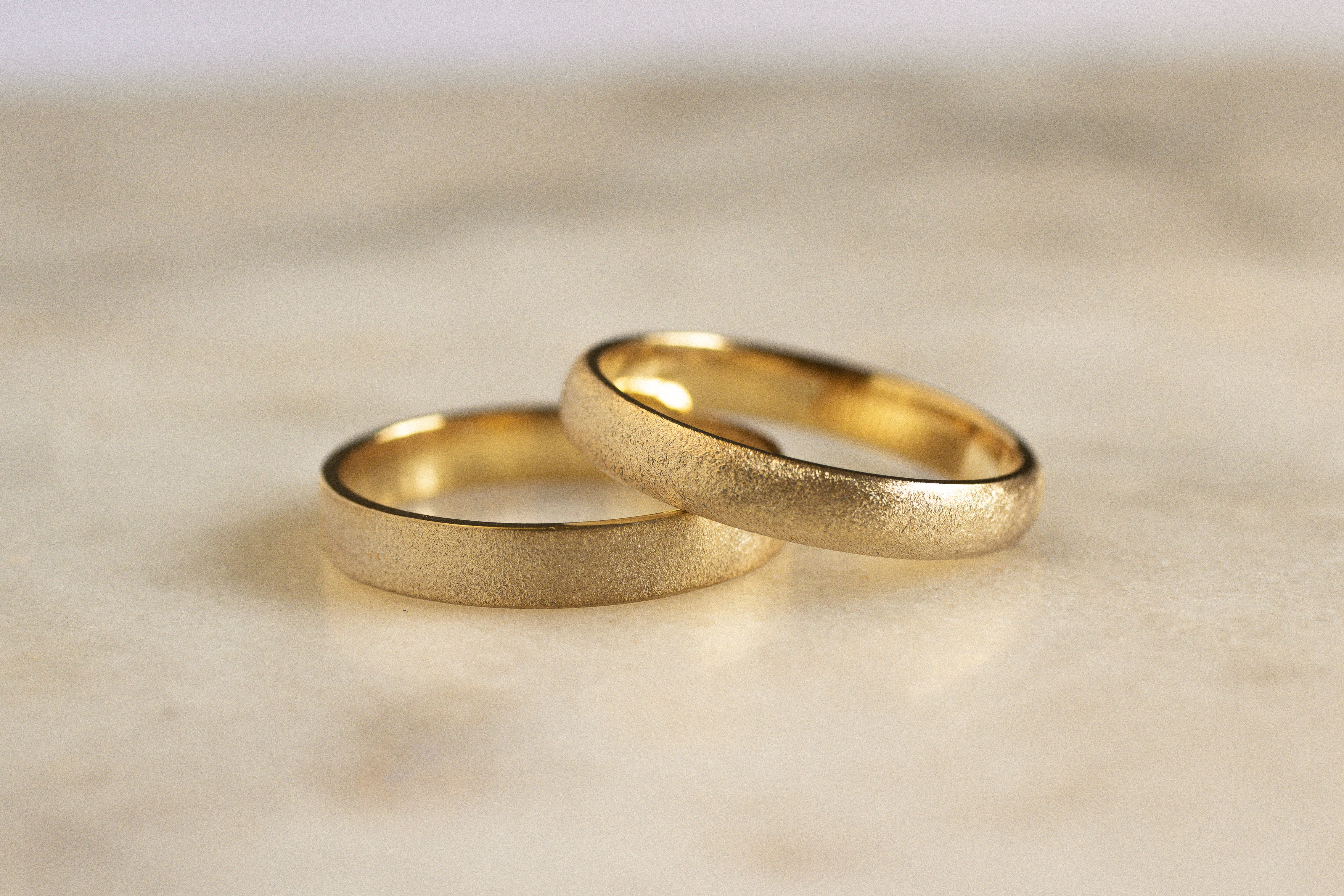 matte gold frosted wedding rings in different shapes on marble surface