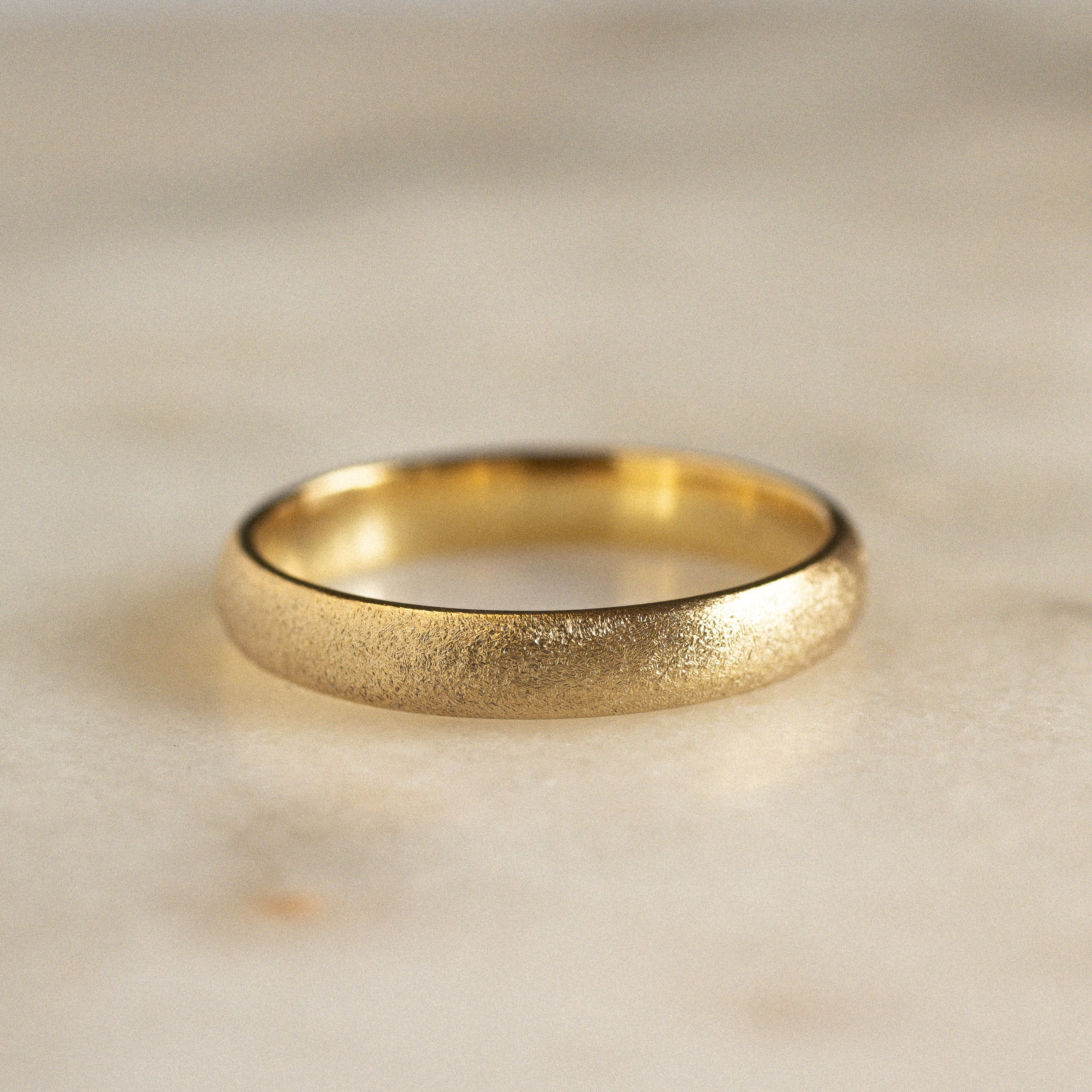 gold matte wedding ring with frosted texture on a marble surface
