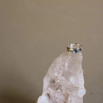 silver topaz ring balancing on top of a white crystal with a beige background