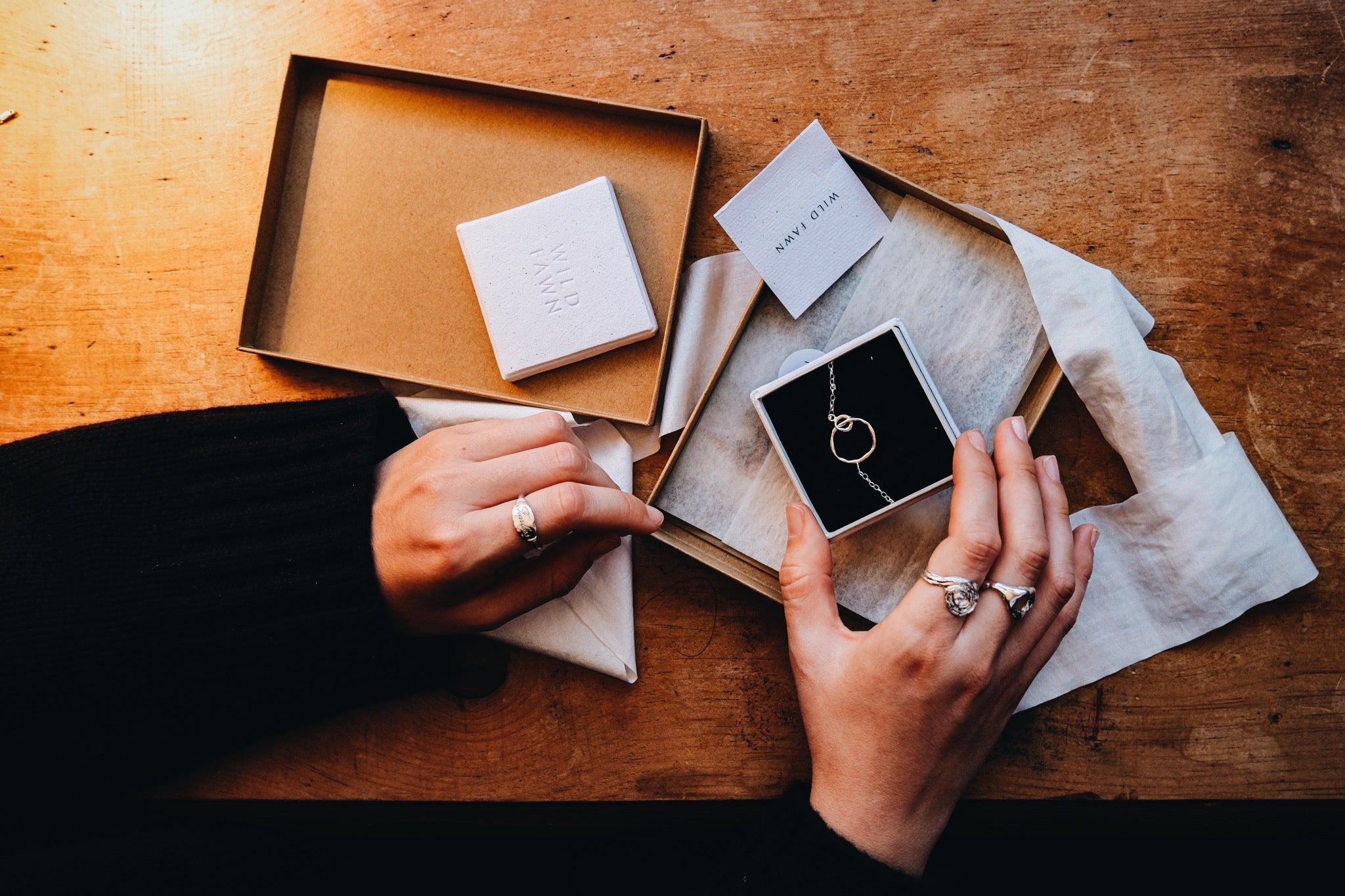 Person holding a jewelry box with a necklace on a wooden table