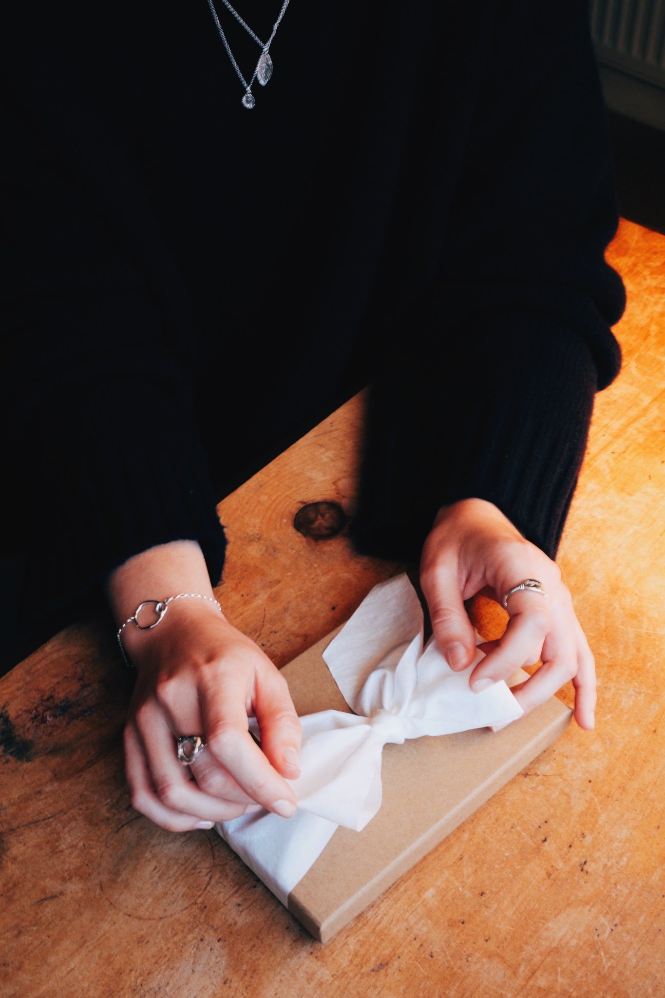 Person tying a white ribbon on a wooden box with a warm light setting.