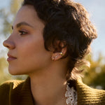 Woman wearing a brown sweater with lace trim, standing outdoors with trees in the background.