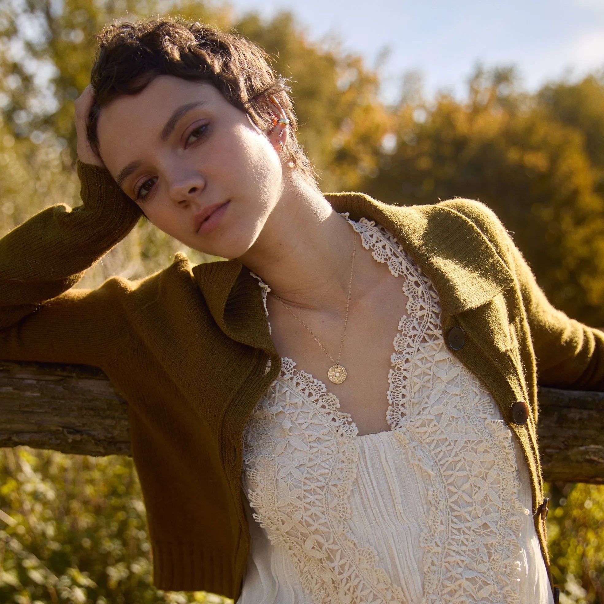 model leaning against a fence wearing lace dress and cardigan wearing gold moonphase necklace