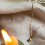 close up of 9ct gold mini acorn necklace with chain and blurred candle in foreground