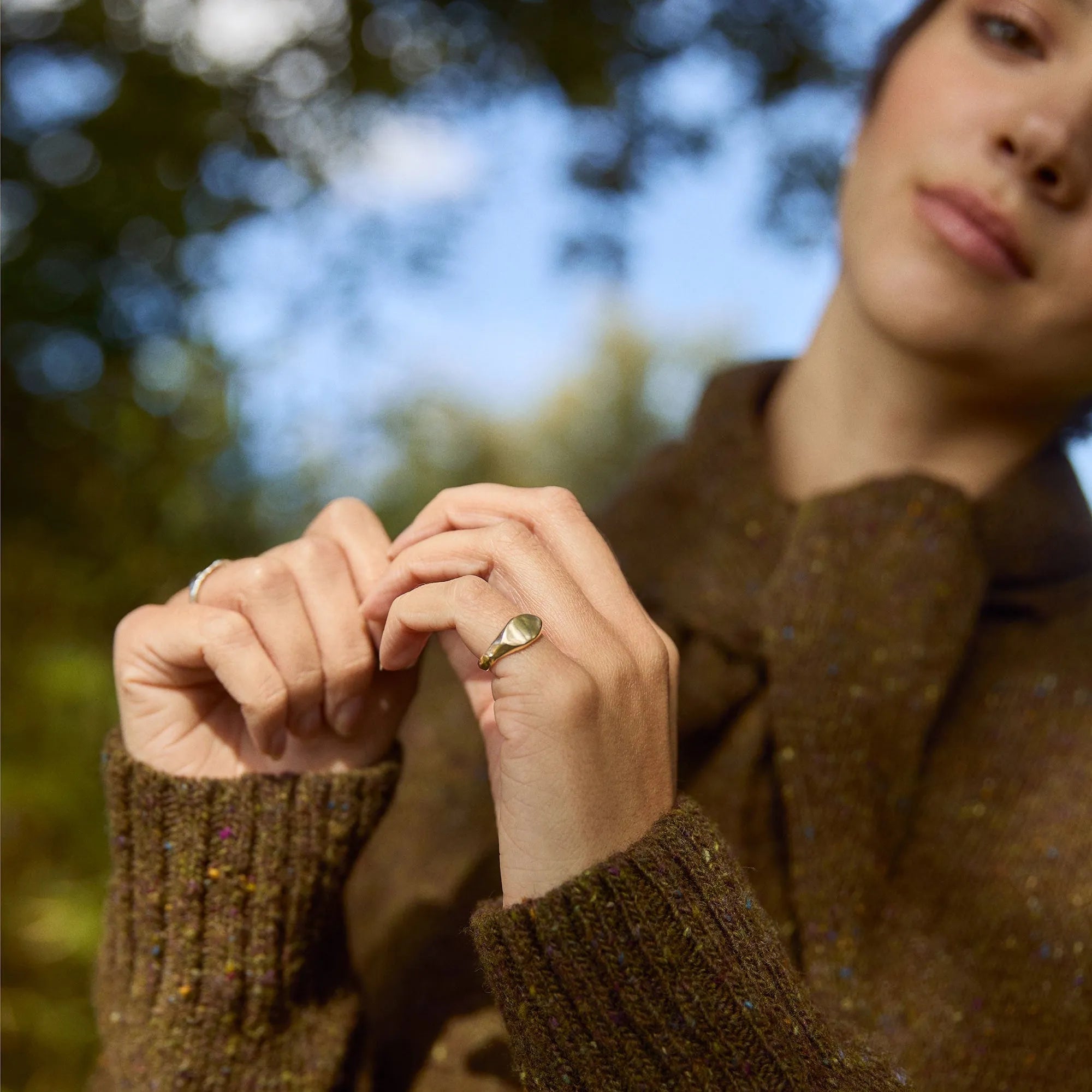 female model outside wearing brown jumper and gold pinkie ring on her little finger