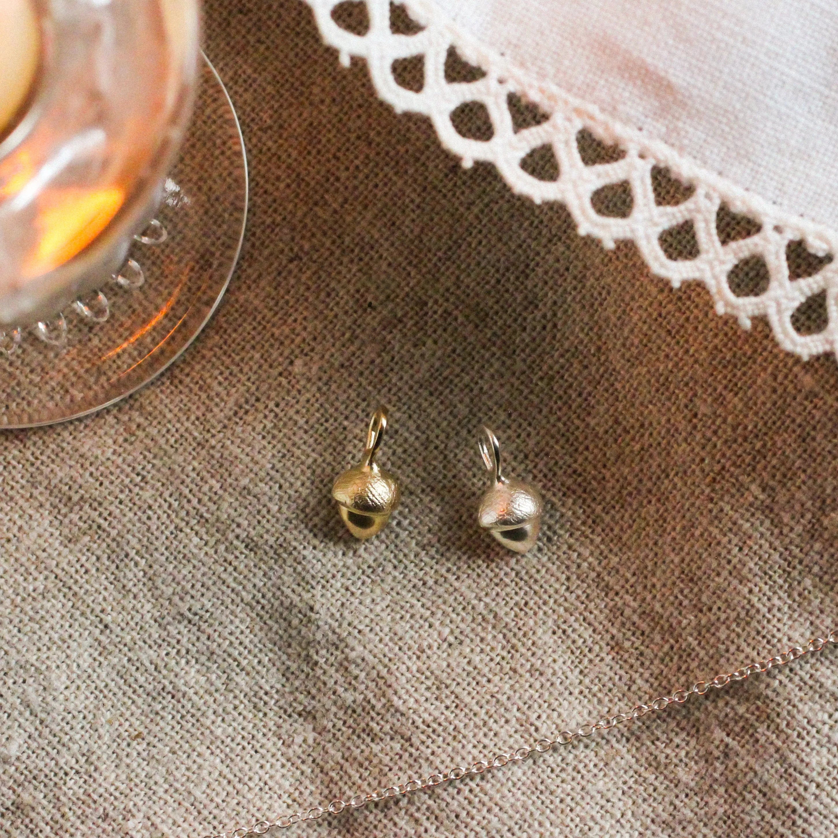 acorn shaped pendants in silver and gold with silver chain, candle and lace fabric