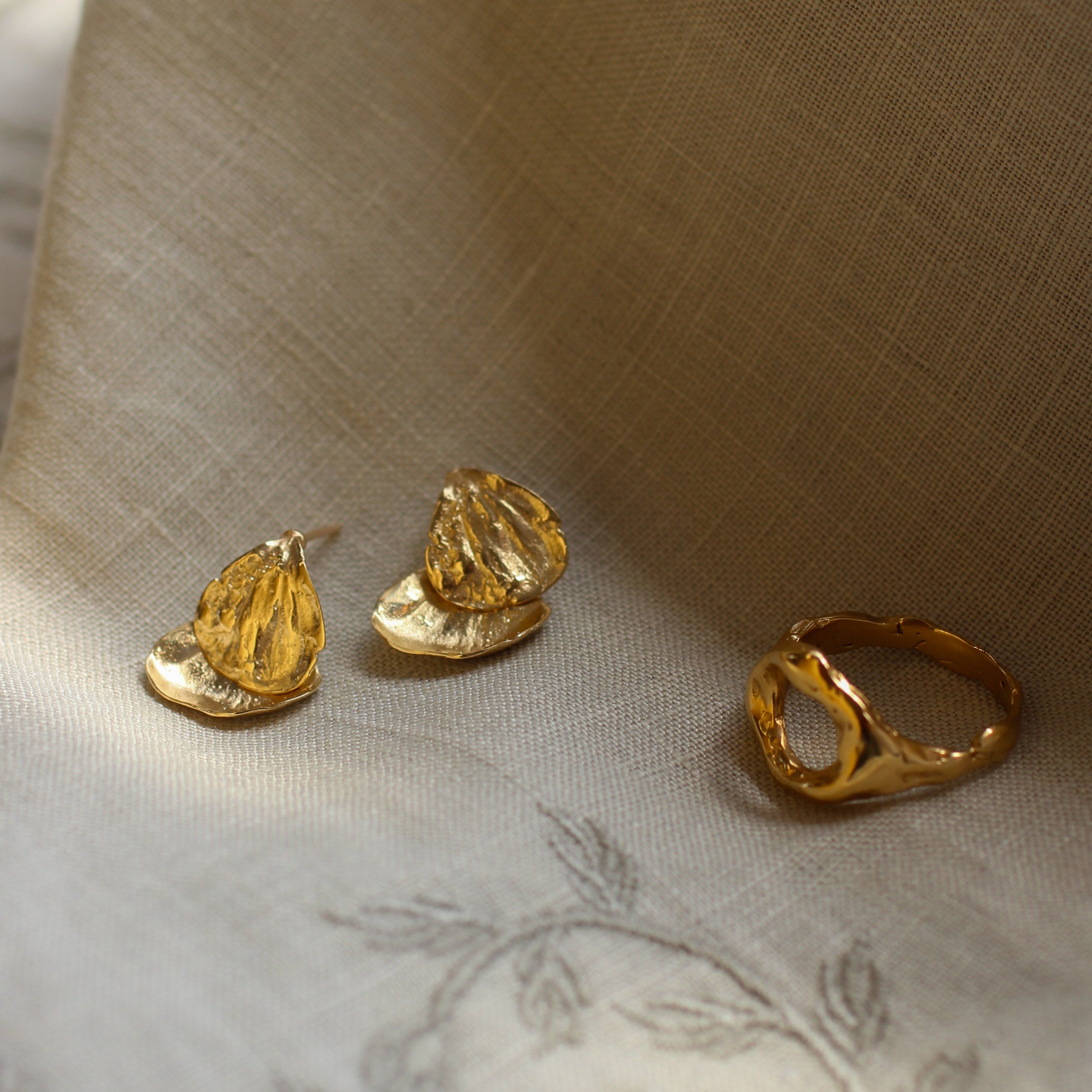 Gold earrings and ring on a textured fabric surface