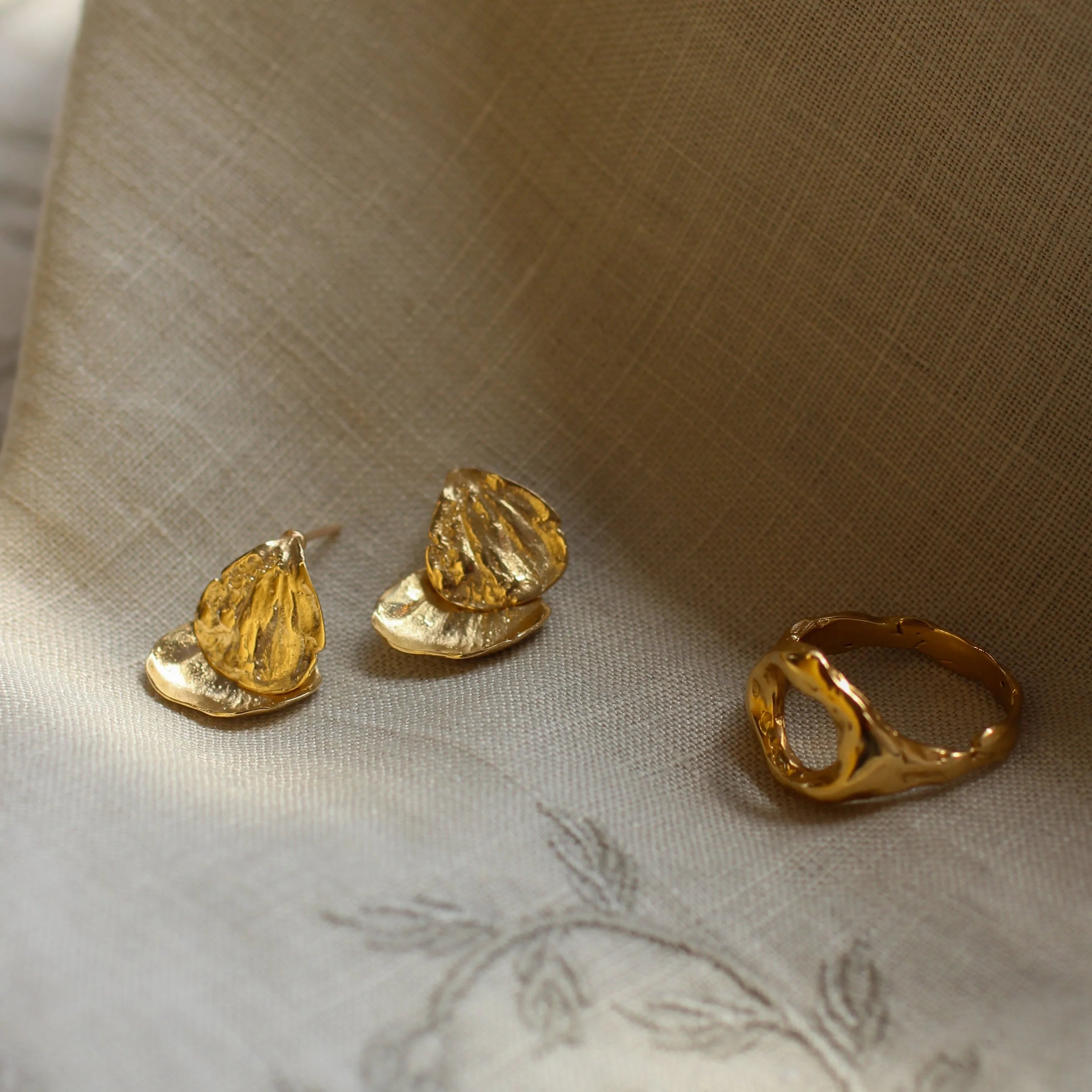 Gold earrings and ring on a textured fabric surface