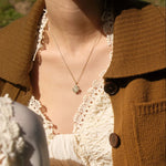 close up of model wearing gold clover necklace with brown cardigan and lace dress in the sunshine