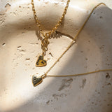 Gold necklace and bracelet with heart-shaped pendants on a textured stone surface