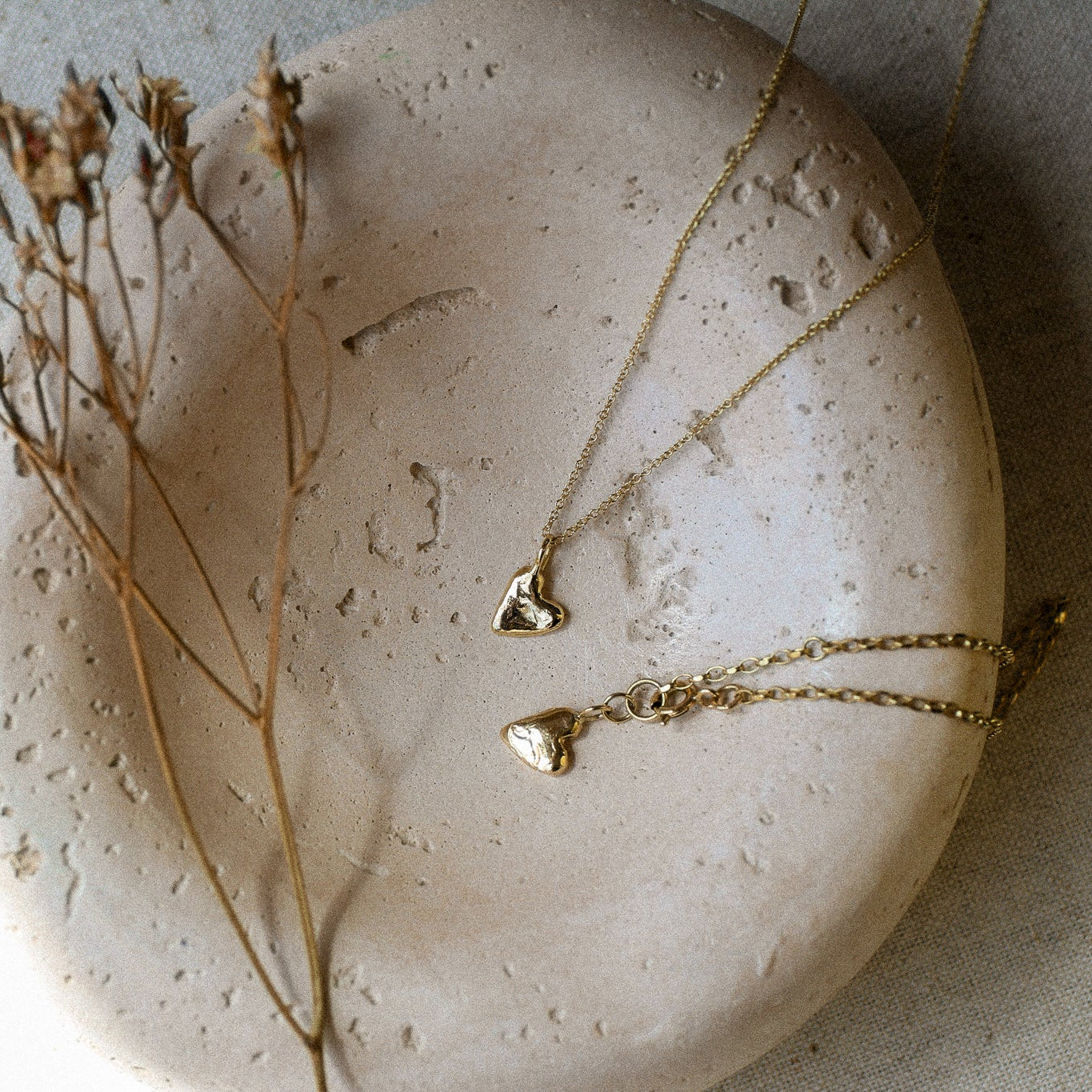 Gold necklace and bracelet with heart pendants on a textured stone surface with dried flowers