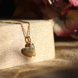 Gold heart-shaped pendant necklace on a textured surface with pink flowers in the background
